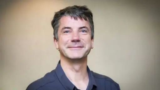 A portrait of a smiling man wearing a blue collared shirt. 