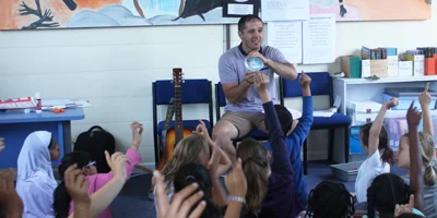 Teacher holding up an inquiry resource (a paua shell) to a class of students with their hands up
