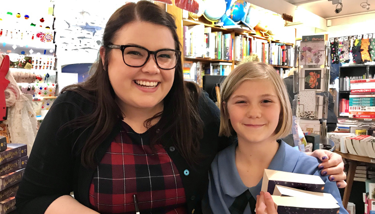Jessica Townsend smiling with her arm around a young reader who is holding some books.