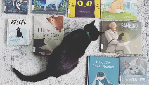 A black cat sitting amongst some children's books.