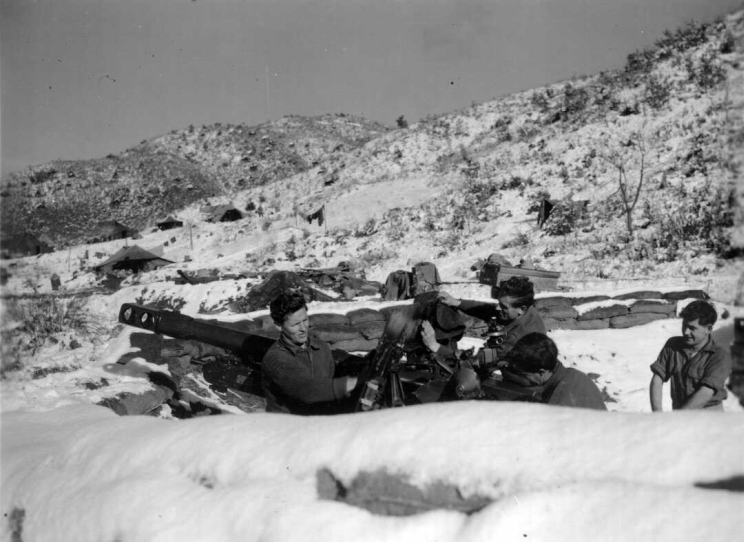Four men seen cleaning a large gun shortly after a heavy snow fall.