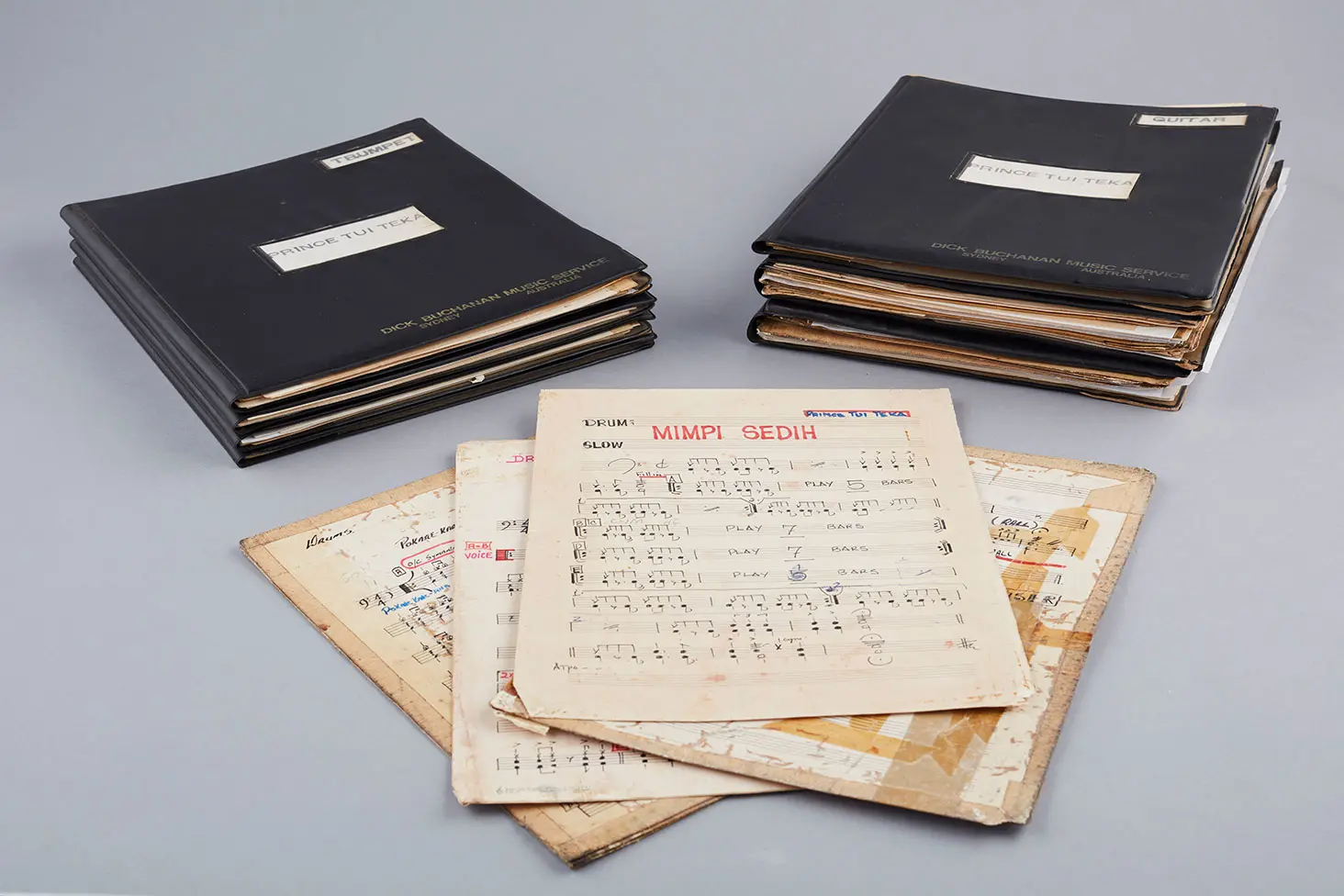 Colour studio photo of musical arrangements by Prince Tui Teka, showing 4 music sheets placed beside 2 folios.
