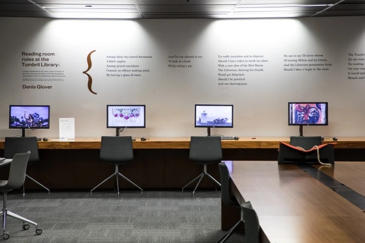 A view of a library reading room with four public computer stations and a poem printed on the wall above them.