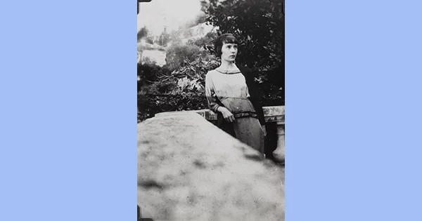 A woman with short dark hair on a verandah with a large tree in the background.