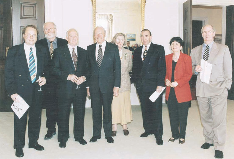 Men, mostly in dark suits, standing along with two women.