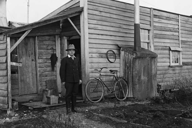 Joseph Divis standing outside his cottage. There is a bicycle leaning against the wall. 