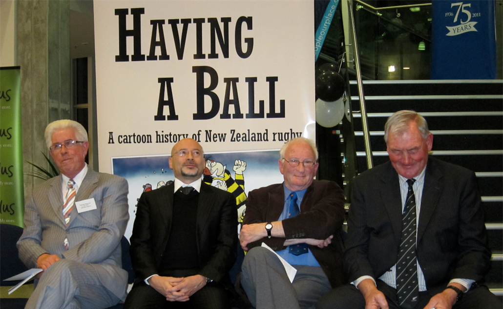 Four men seated together in front of a large poster for the book 'Having a Ball'.