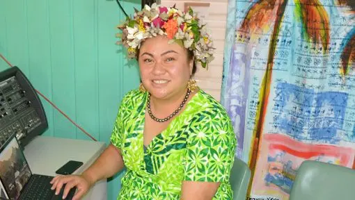 A woman is seated behind a laptop at a small table wearing a colorful ei katu, flower crown. 
