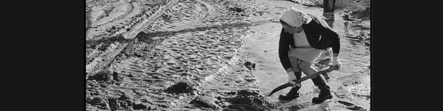 A woman shovelling mud after a flood. 