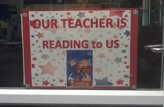 A sign on a window that says 'Our teacher is reading to us'.
