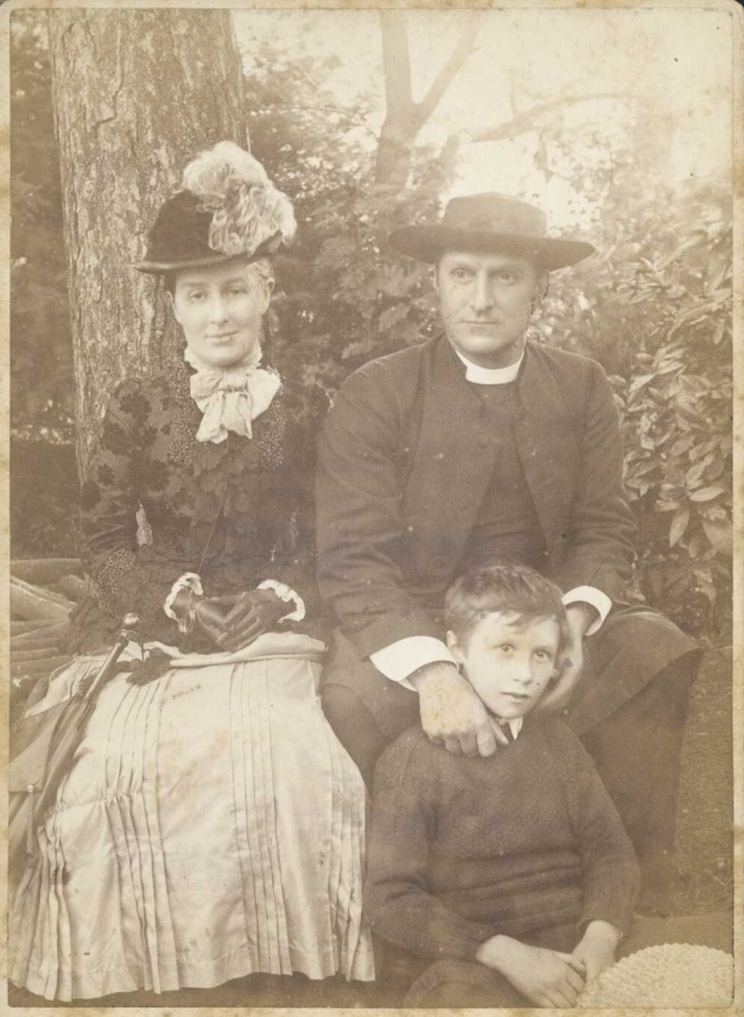 Portrait of a young family, a young boy is seated on the ground in front of his father.