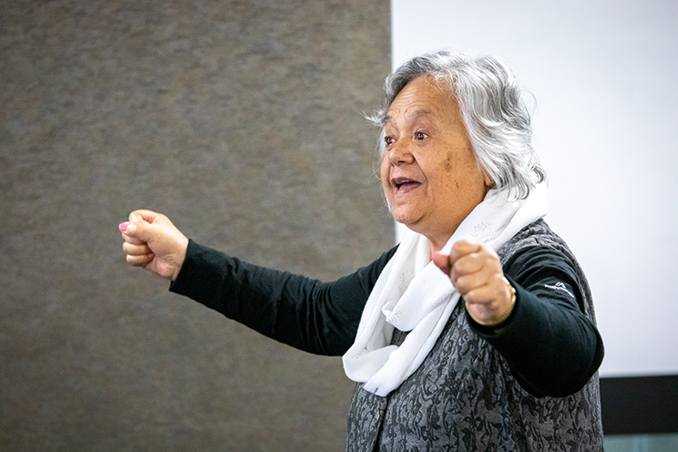 Older Māori woman speaking with her arms akimbo. 