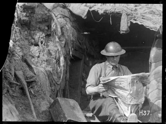 A WW1 soldier reading a newspaper in the front line trenches.
