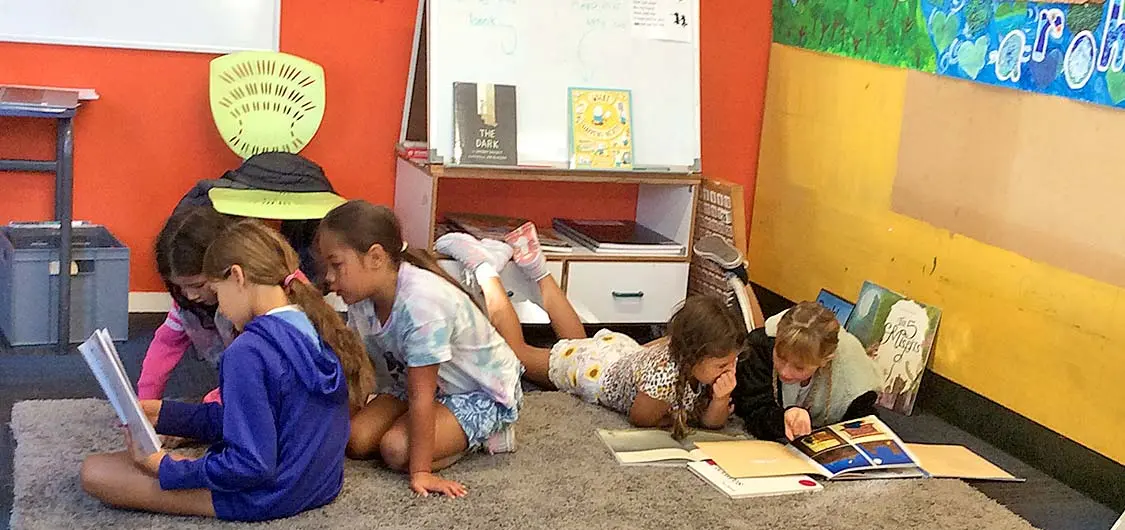 A group of tamariki reading picture books together on a classroom floor.