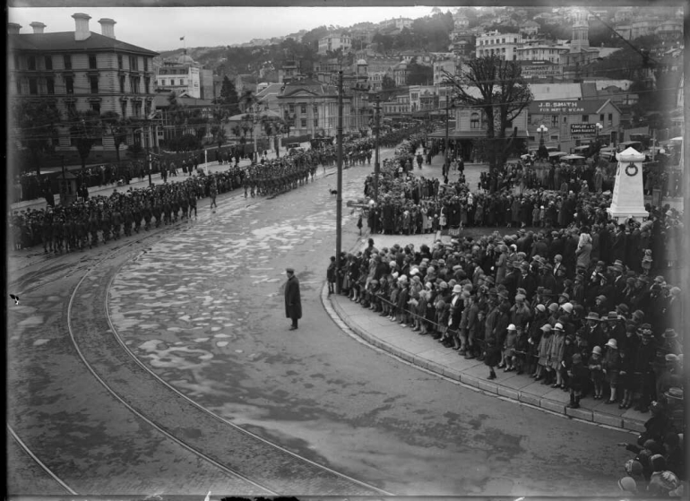 Looking south along Lambton Quay as the parade marches down the street which has been cleared. Crowds line the footpaths.