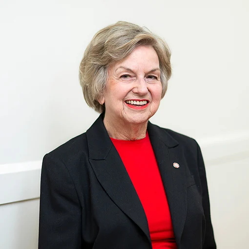 Photo of a smiling woman wearing a black blazer and a red top.