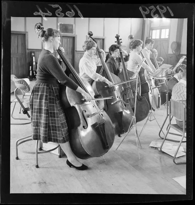 Line of six people playing the cello in an orchestra. 