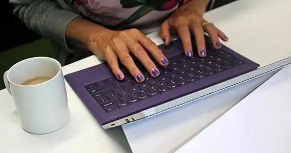Person wearing purple nail polish typing on a purple keyboard.