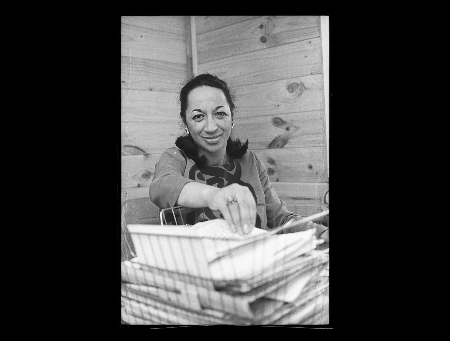 Black and white photo of Whetu Tirikatene-Sullivan smiling and holding out her hand to grab some papers.