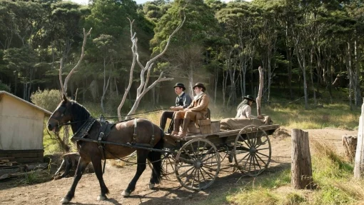 A horse-drawn cart carries three men, two seated up front and one at the back.