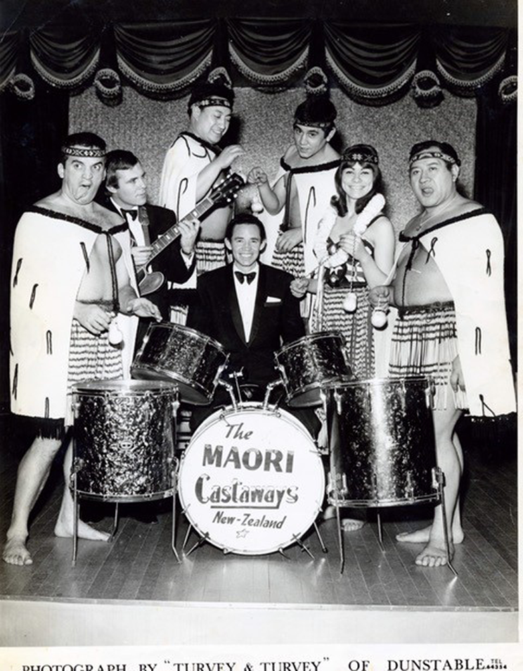 A gorup of Māori performers standing around a drumkit.