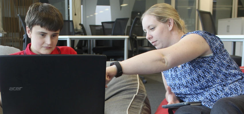 Female teacher helping young male student with a laptop.