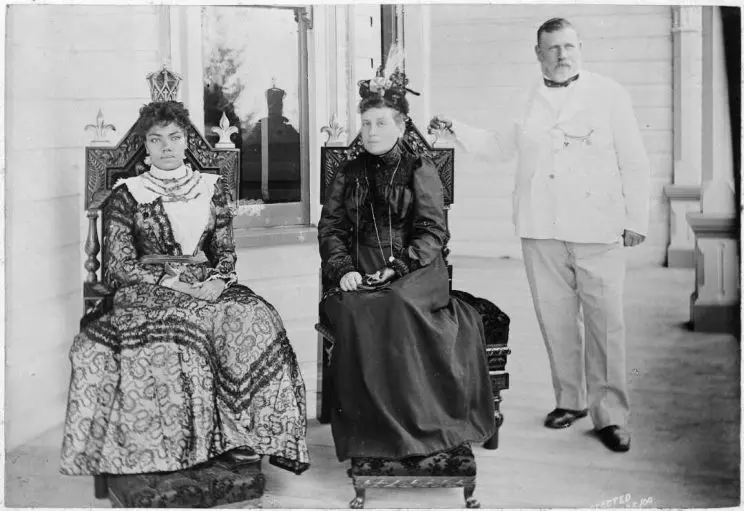 A black and white portrait of three people, two women are seated and a man stands beside them. 