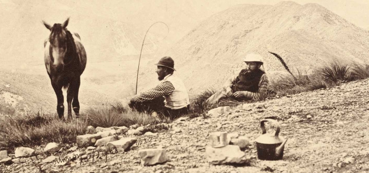 Two men appear to stop for tea along a rocky road high in the mountains, their horse is also shown in the frame.