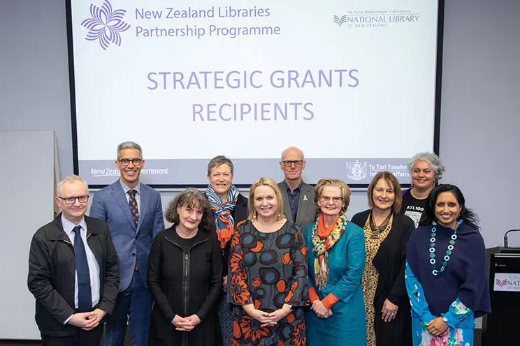 Group of men and women standing in front of a slideshow titled "Strategic Grants Recipients"