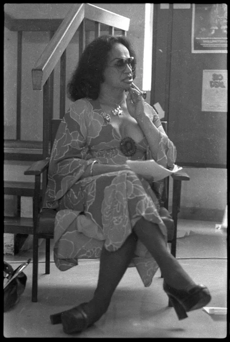 Black and white photo of a woman wearing a flowery dress and sunglasses. 