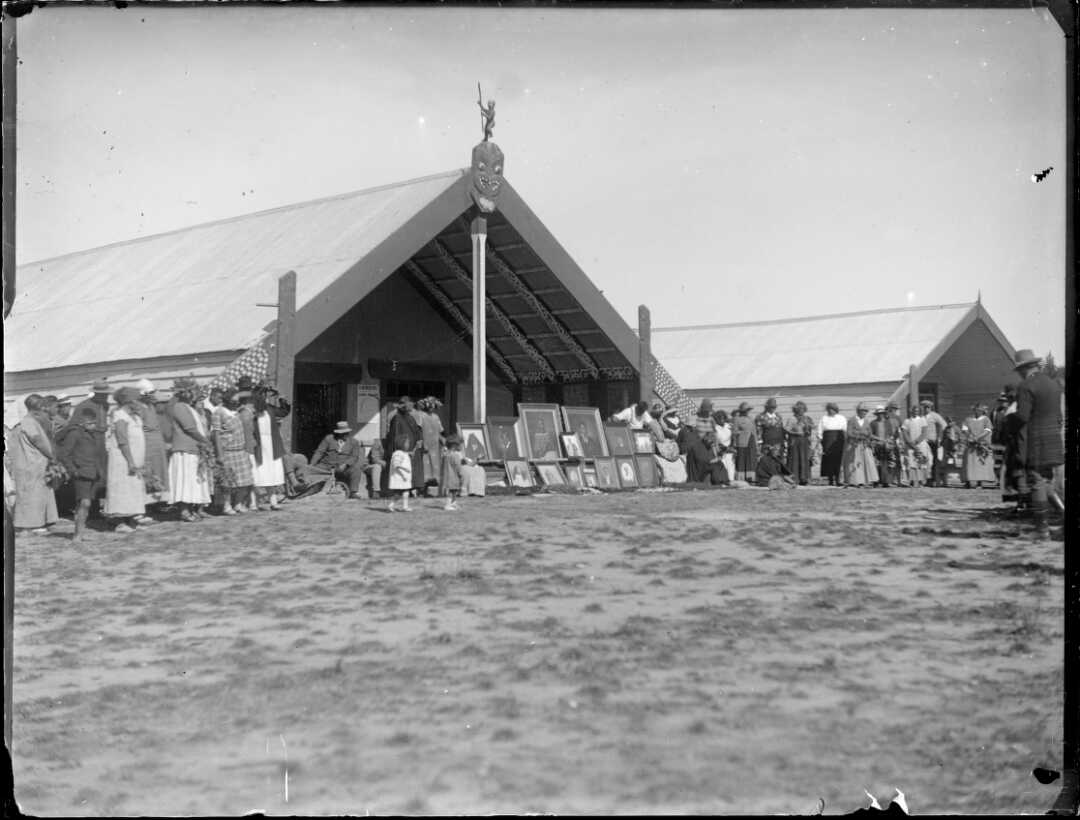 Black and white photo of people standing outside a large marae.