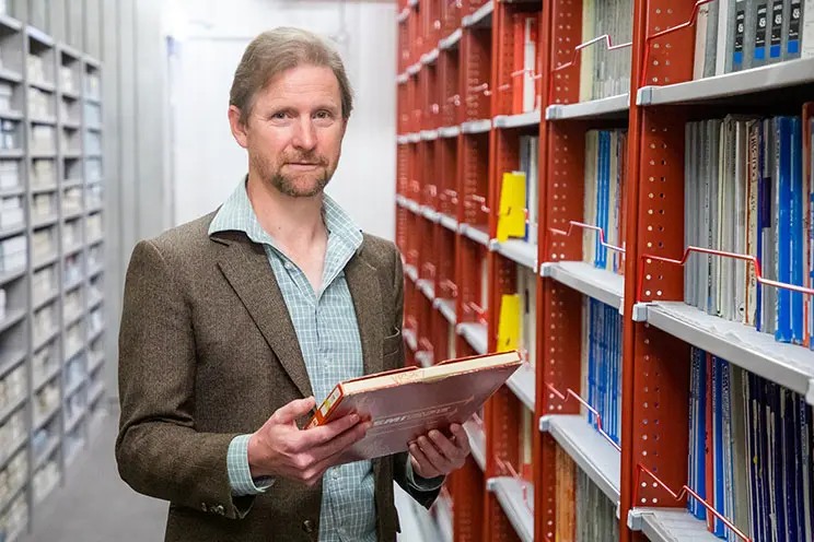 A man standing between lots of shelving holding a record.