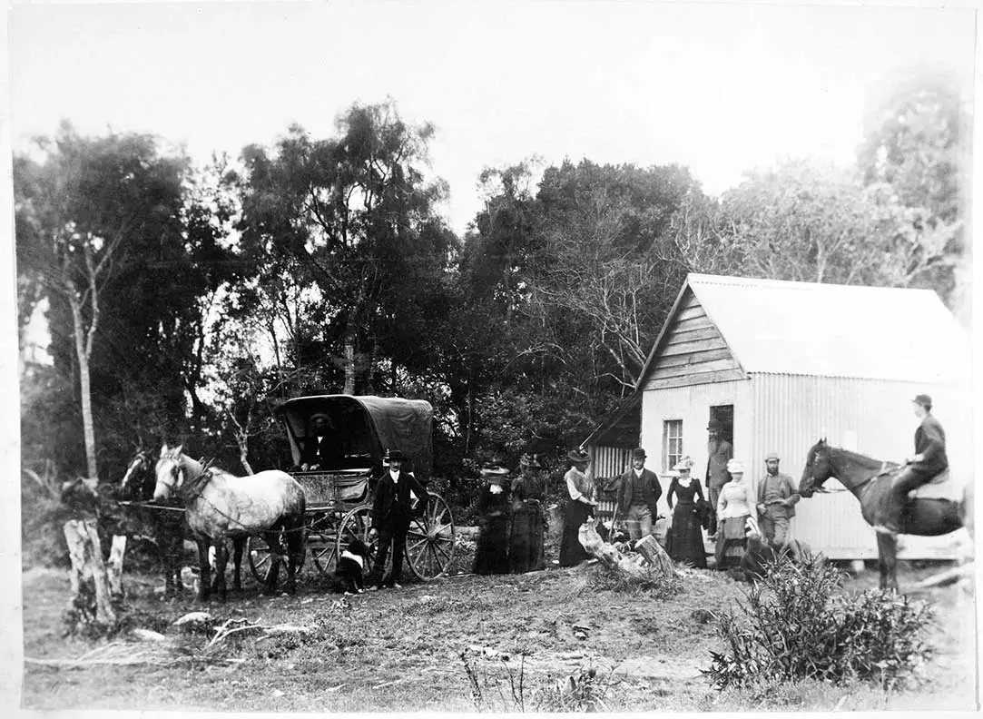 Black and white photo of a group of women and men, a horse and carriage, and a man on a horse outside a small building in Tahakopa.