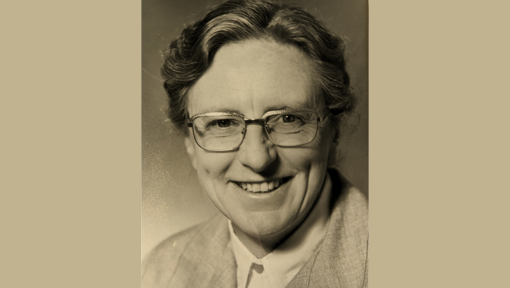 A black and white portrait of a smiling woman wearing glasses. 