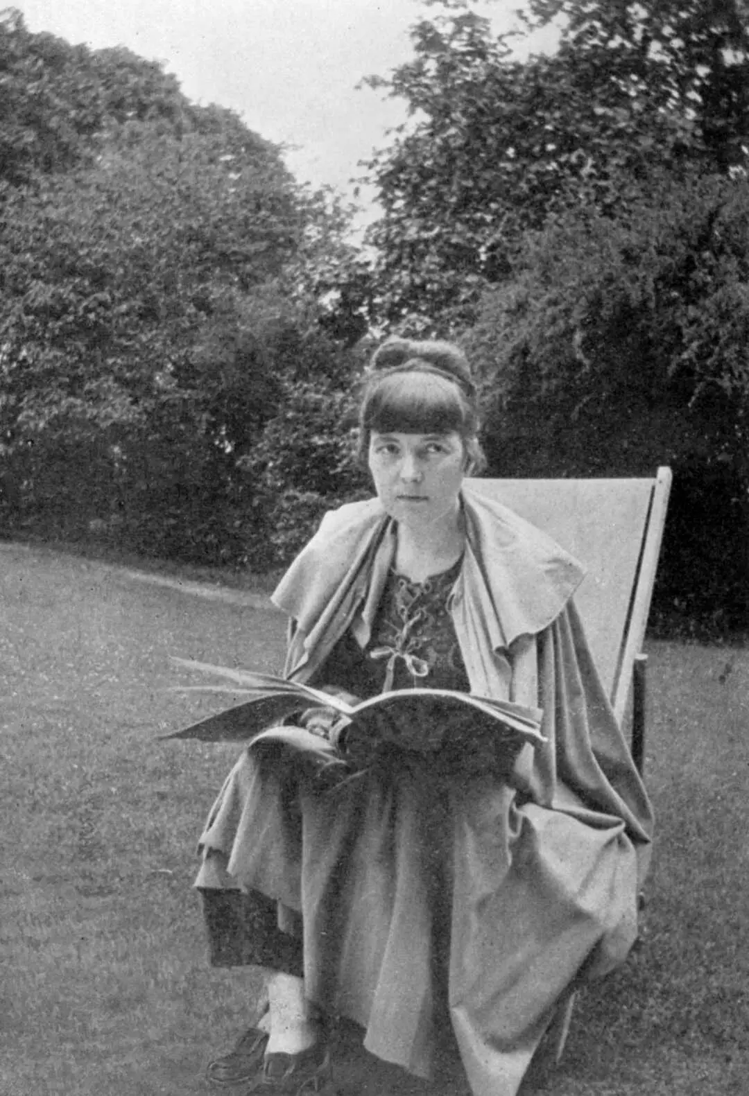 Katherine Mansfield sitting in a chair outdoors with a magazine or book in her lap