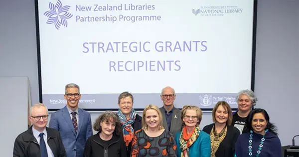 Group of men and women standing in front of a slideshow titled "Strategic Grants Recipients"