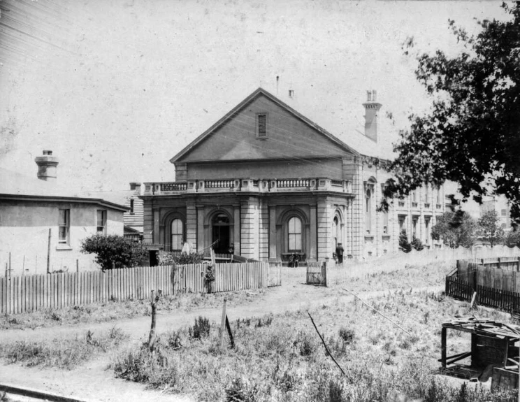 A black and white photo of a wooden single story building with an empty lot next to it.