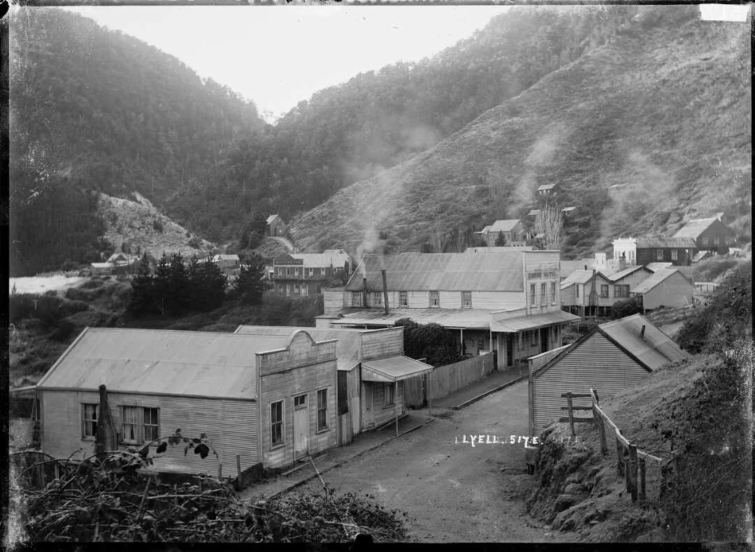 A view of a small town with dirt main street and smoke coming from the various chimneys.  