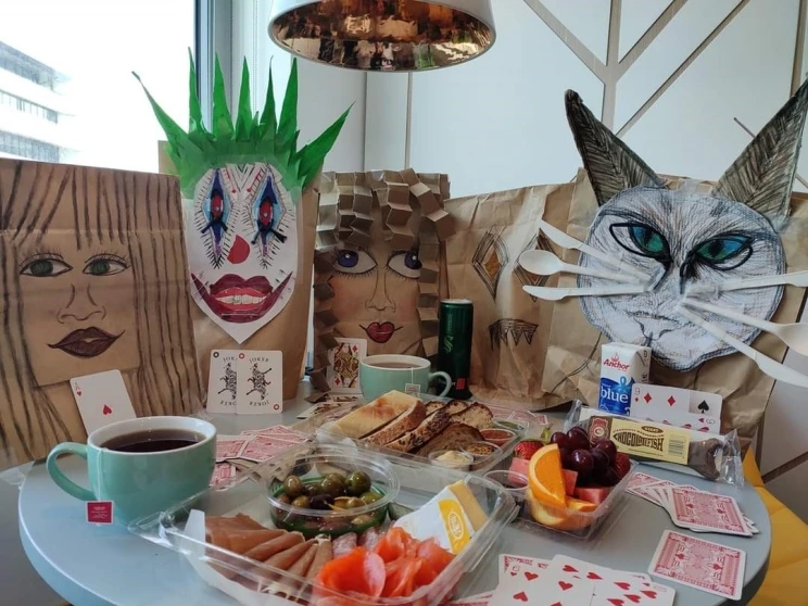 A picnic laid out on a table with food and playing cards with attendees made of paper cutouts.