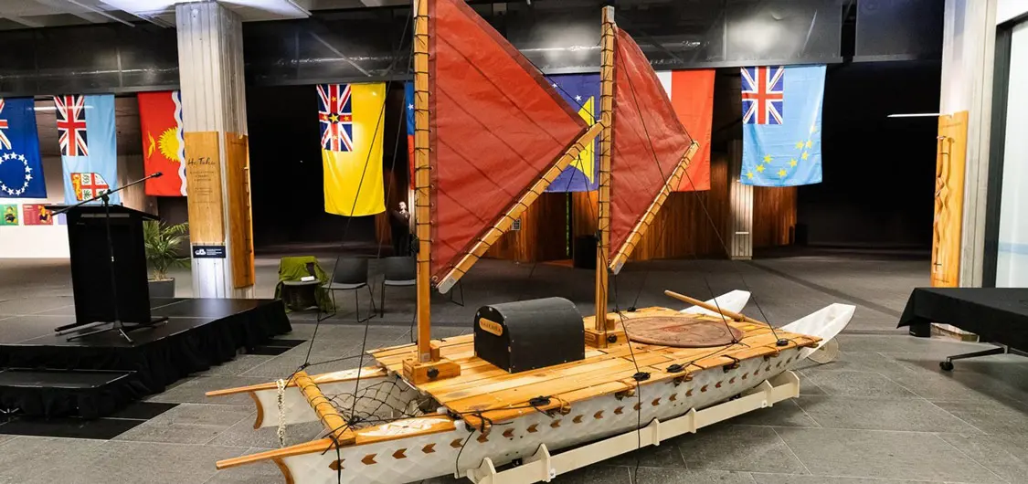 The replica voyaging waka 'Whakaura' on display at the National Library in Wellington with Pacific flags hanging in the background.