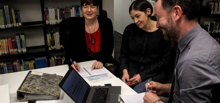 Three school staff holding a summer reading planning meeting in a library.