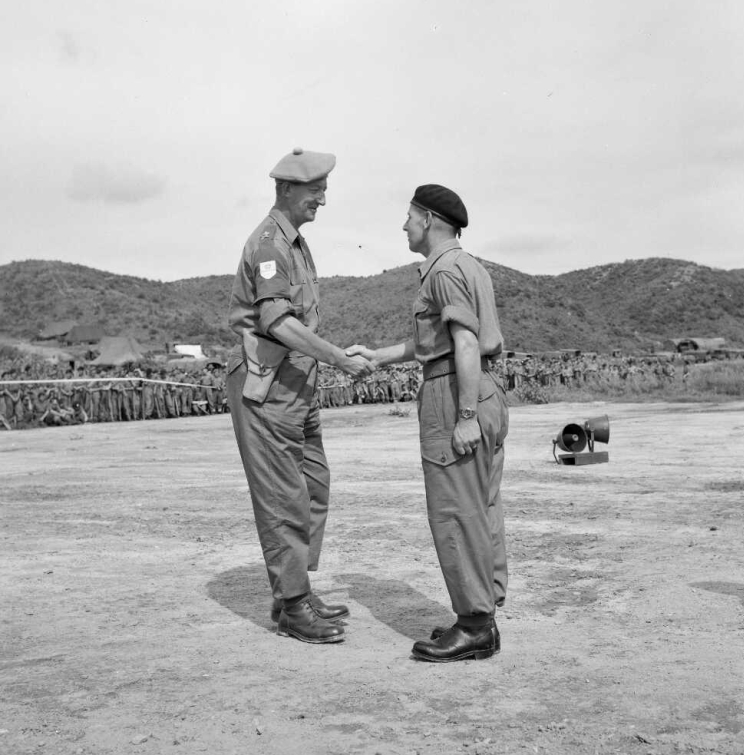 Two men in military uniform shake hands during a ribbon pinning ceremony.