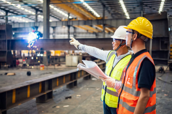 Two men pointing at industrial machinery in factory