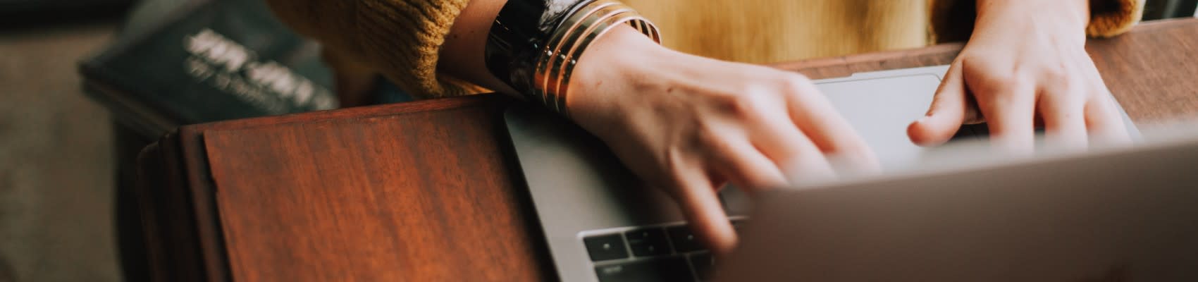 A woman typing using her laptop on a wooden desk.