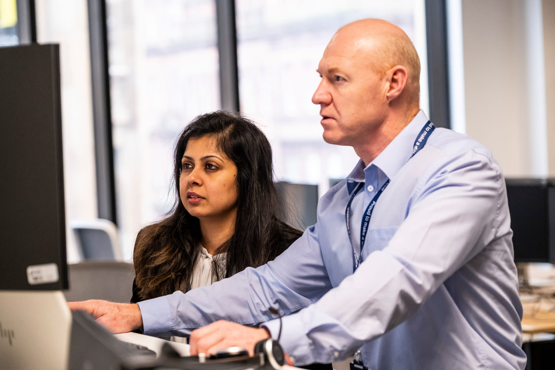 Bald man in shirt with woman in suit, in an office setting