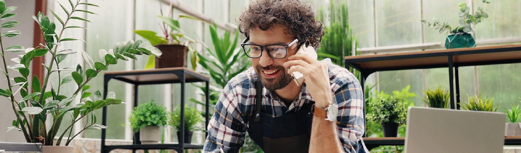 A man in agricultural garb in what appears to be a greenhouse and foliage surrounding him