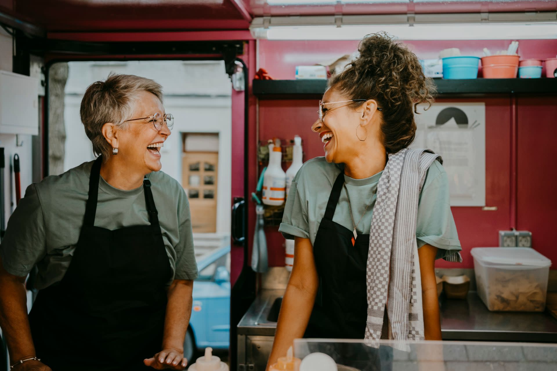 Two ladies laughing while in a kitchen, preparing food.