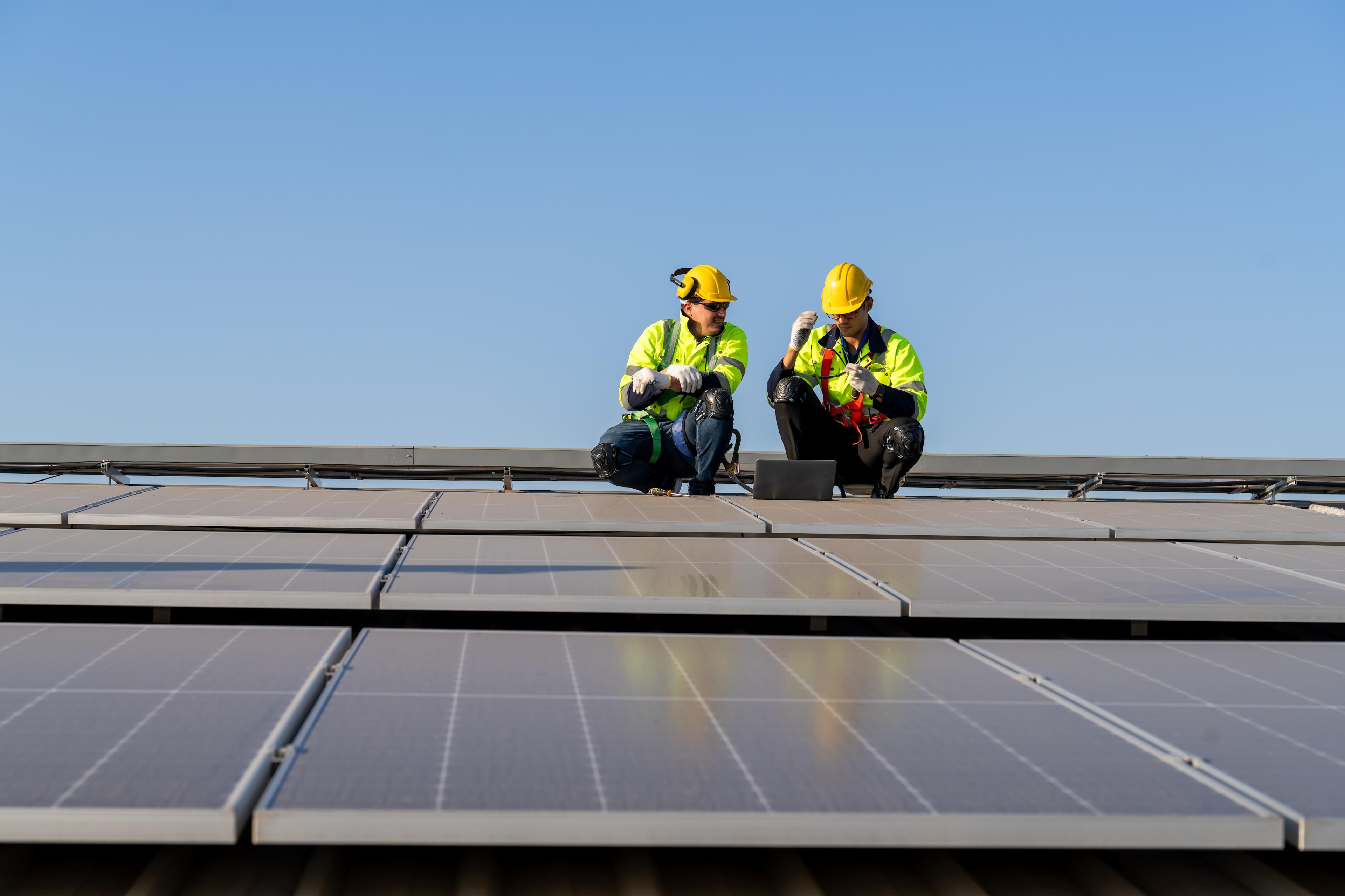 Two engineers in safety gear sitting on a solar panel roof.