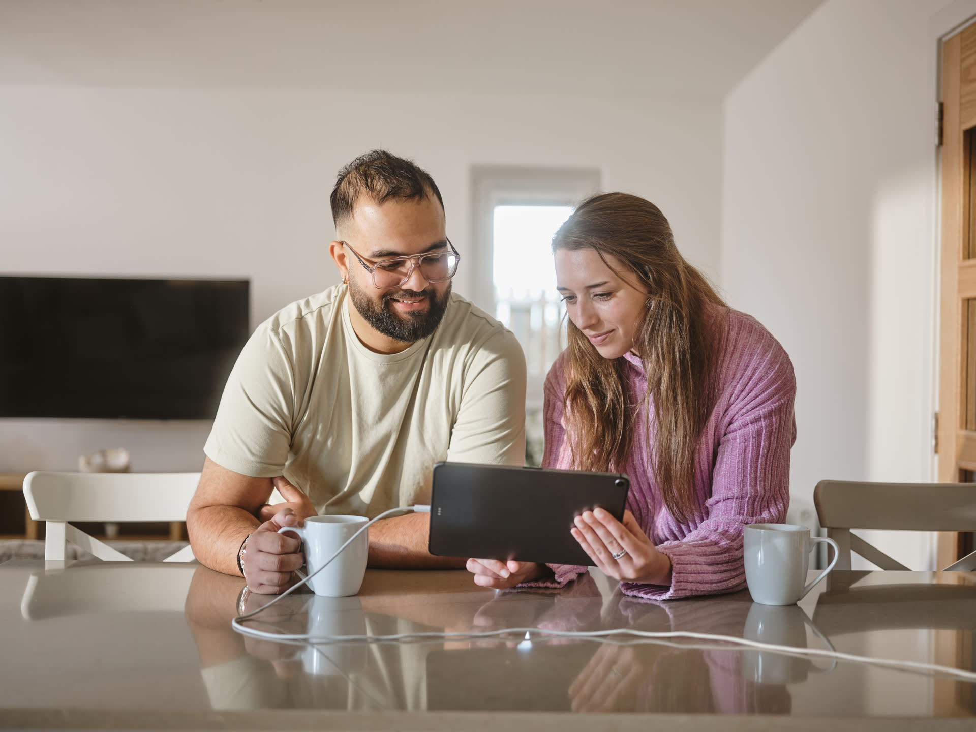 A man and woman, sat at a counter in their home, looking at a tablet
