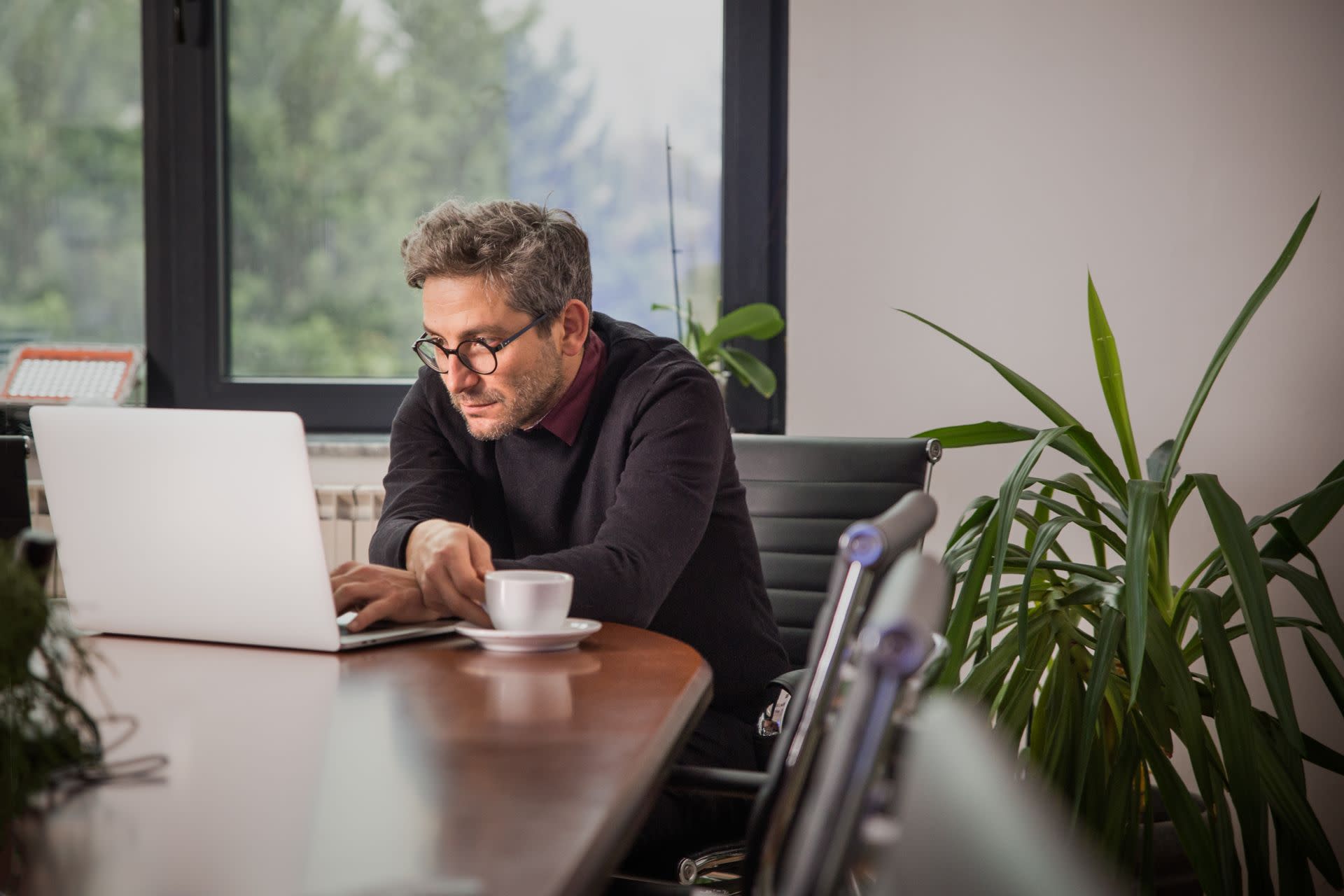 A man sits hunched over a laptop in an office setting